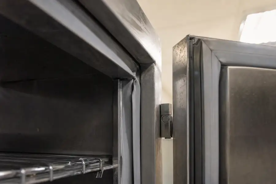 High-detail documentary for “Commercial Refrigerator Door Not Sealing: Work Out Why in Five Minutes.” Show a light-leak photo taken from inside a cabinet. Focus on the gasket profile, mitre, magnetic strip, retaining channel, hinge, latch, measurement point or visible failure pattern that supports the article’s explanation. Relevant equipment: Reach-in coolers and freezers; prep tables; undercounter units. Relevant manufacturers when naturally visible: Contextual. Realistic commercial-kitchen surfaces, accurate proportions, no added labels or text, horizontal composition.