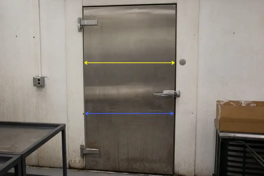 Editorial hero photograph for a commercial foodservice refrigeration article titled “Dart to Dart or Outside Edge: Why Two Suppliers Quote Different Sizes.” Show Same door, two annotated measurements. Relevant equipment: Reach-ins; prep tables; walk-in swing doors; merchandisers. Relevant manufacturers when naturally visible: True as the worked dart-to-dart example. Use an authentic restaurant, grocery, school-kitchen or foodservice setting, natural practical lighting, realistic wear and materials, documentary composition, no staged corporate poses, no added text, 16:9 landscape. When the brief requires technical proof, publication should use a real job-site photo instead of an invented representation.