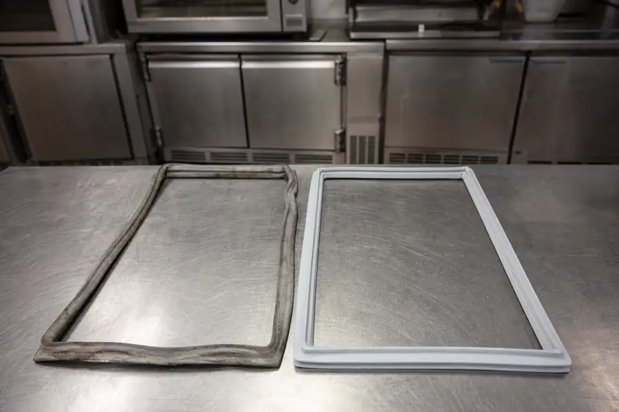 Editorial hero photograph for a commercial foodservice refrigeration article titled “OEM, Aftermarket or Custom Cut: Choosing a Commercial Gasket.” Show Side-by-side OEM and custom fabricated gasket. Relevant equipment: All unit types. Relevant manufacturers when naturally visible: True, Traulsen, Turbo Air, Delfield as OEM reference points. Use an authentic restaurant, grocery, school-kitchen or foodservice setting, natural practical lighting, realistic wear and materials, documentary composition, no staged corporate poses, no added text, 16:9 landscape. When the brief requires technical proof, publication should use a real job-site photo instead of an invented representation.
