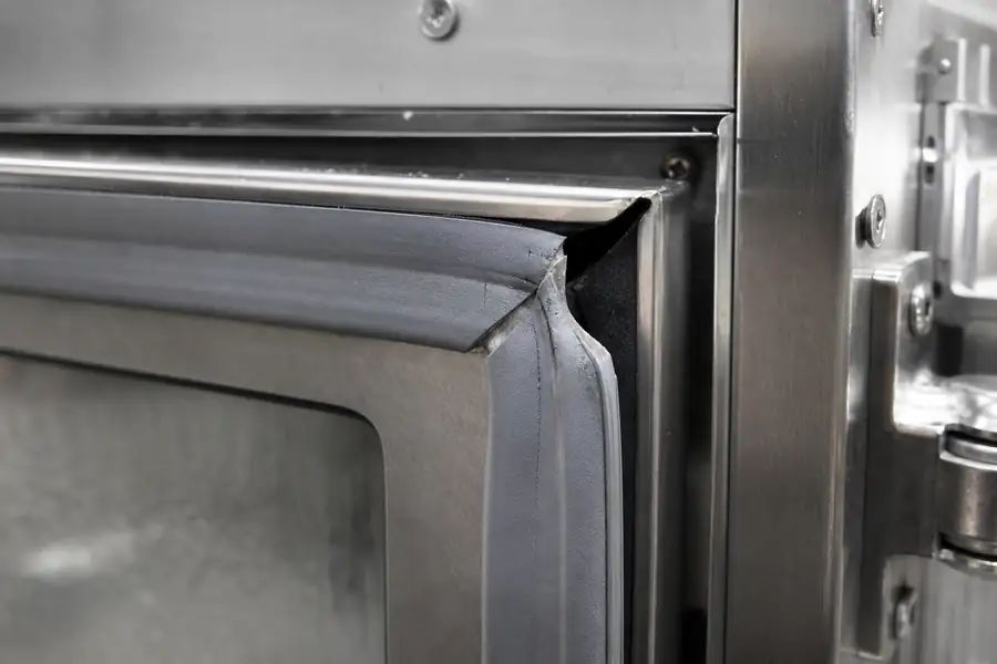 High-detail documentary for “Why Front Range Kitchens Lose Door Seals in Summer.” Show a shrunken gasket showing a corner gap. Focus on the gasket profile, mitre, magnetic strip, retaining channel, hinge, latch, measurement point or visible failure pattern that supports the article’s explanation. Relevant equipment: Walk-ins; reach-ins; glass display. Relevant manufacturers when naturally visible: Contextual. Realistic commercial-kitchen surfaces, accurate proportions, no added labels or text, horizontal composition.